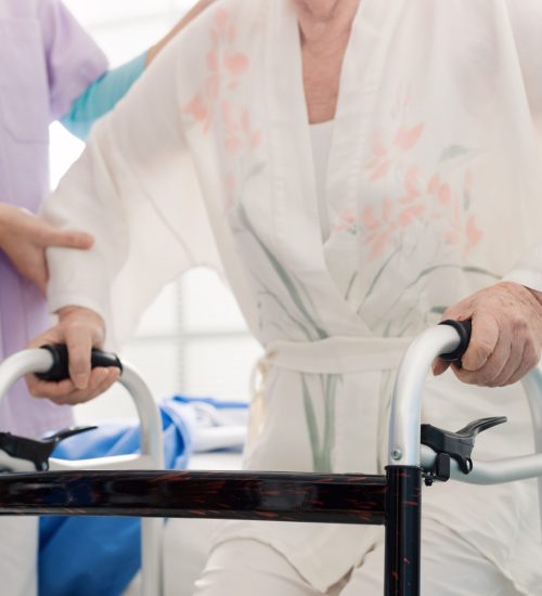Caregiver assisting a senior lady at the retirement home, the woman is leaning on a walker